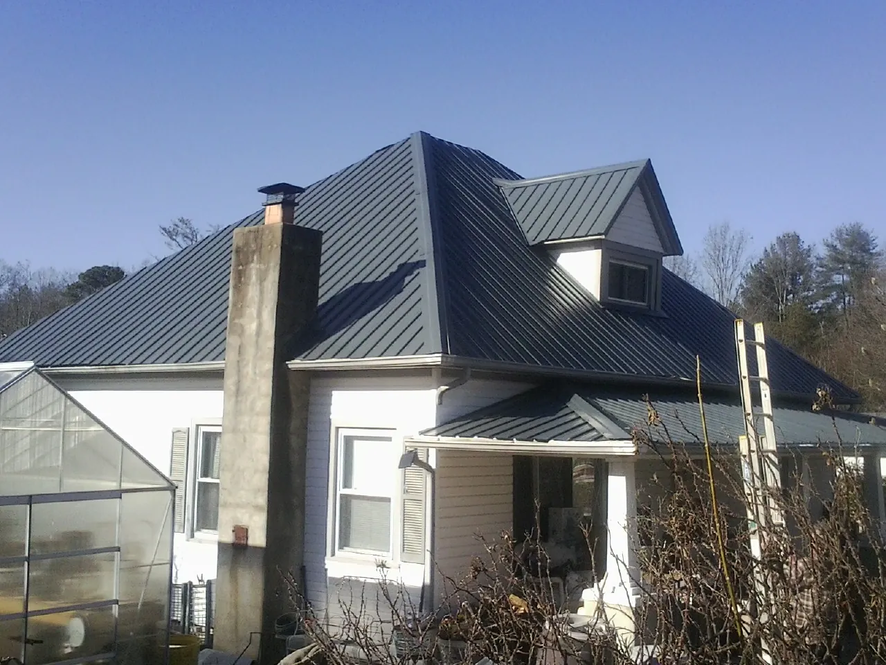 Dark blue standing seam metal roof on a white farmhouse with dormer — Slate & Tile Roof Repair by Roofing Brothers in Rockledge