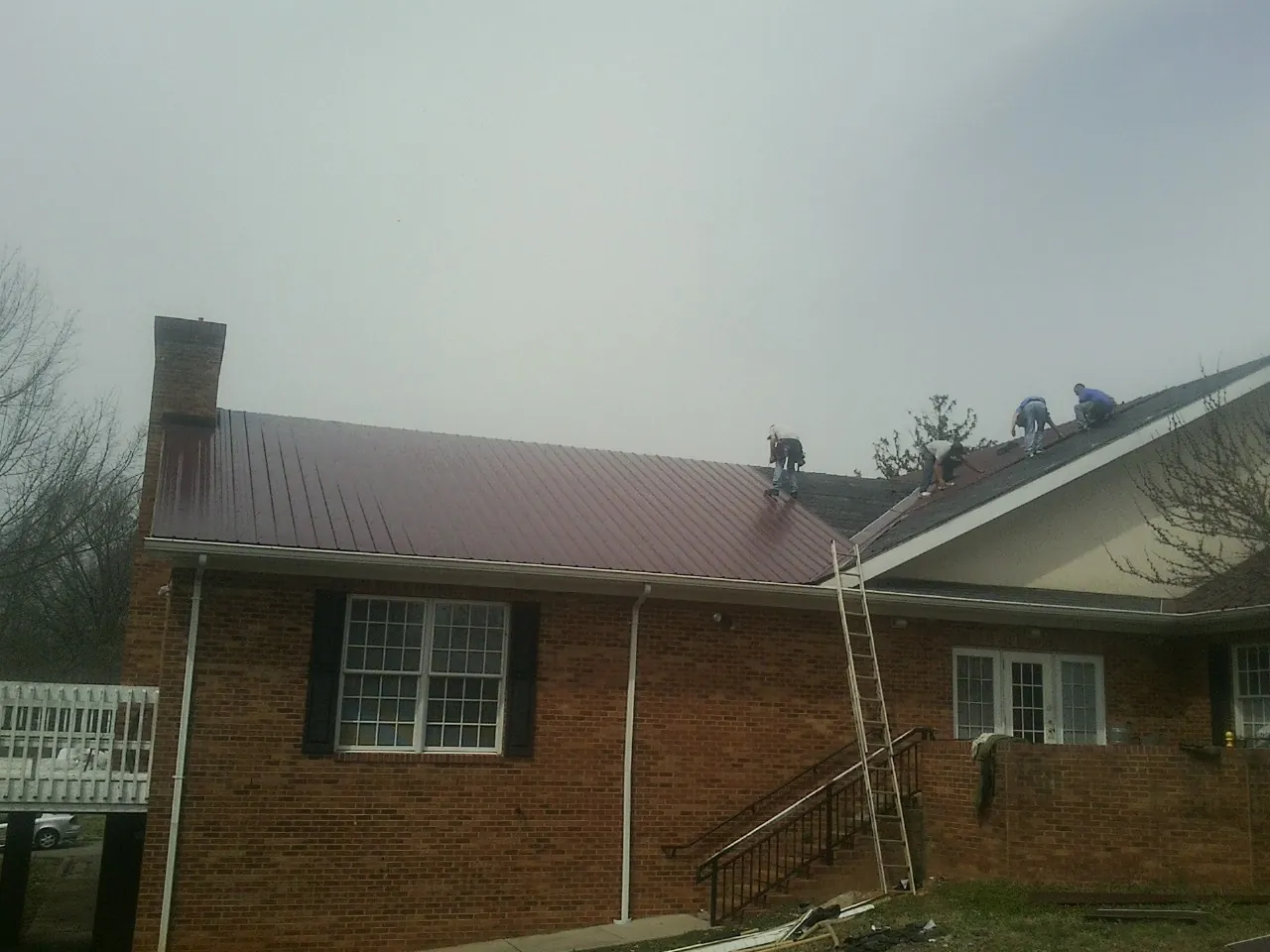 Crew setting red metal roofing panels on a brick home in Rockledge