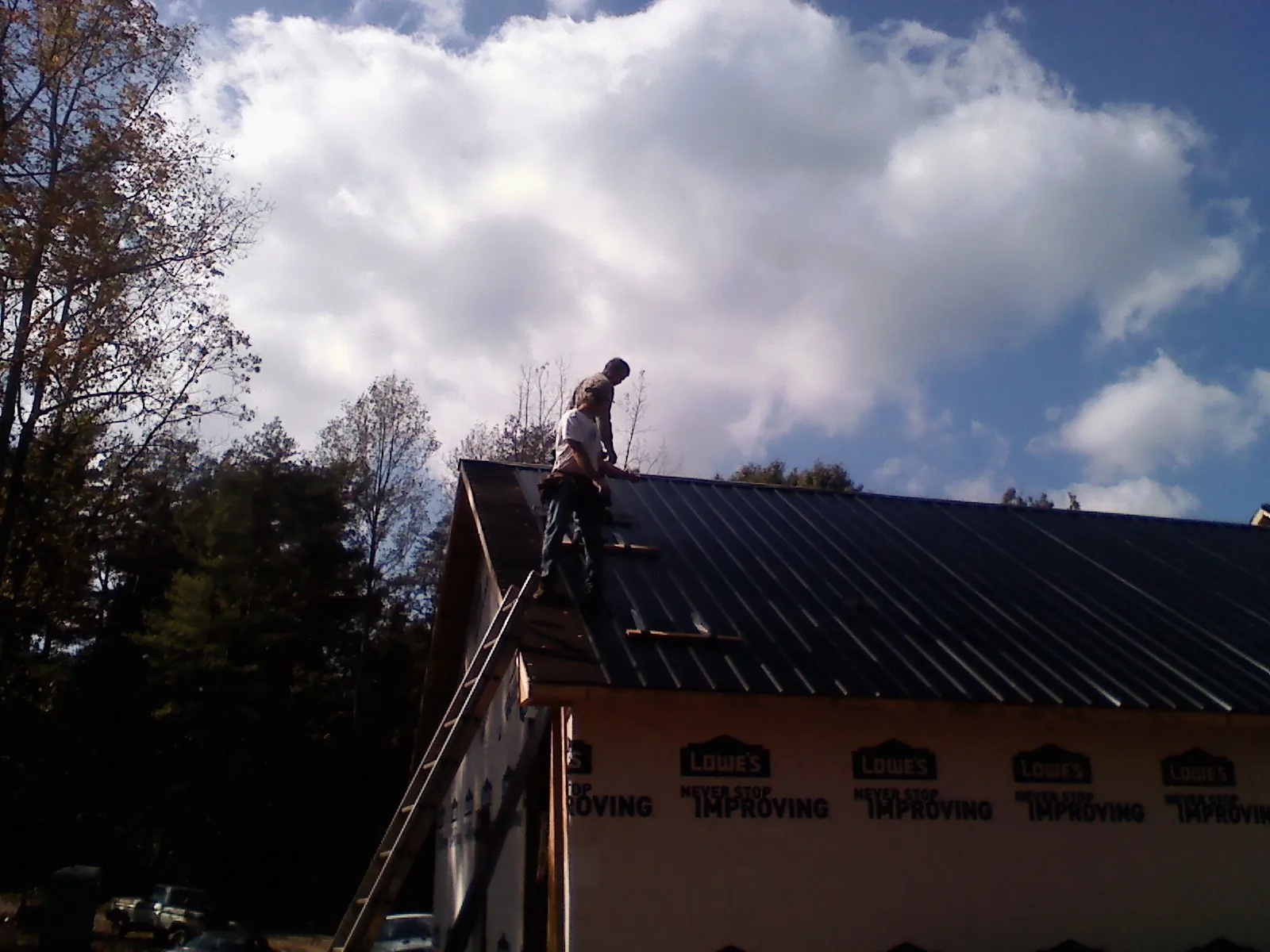 Roofer fastening dark metal panels high against a cloudy sky, from a Roof Inspection job in Rockledge